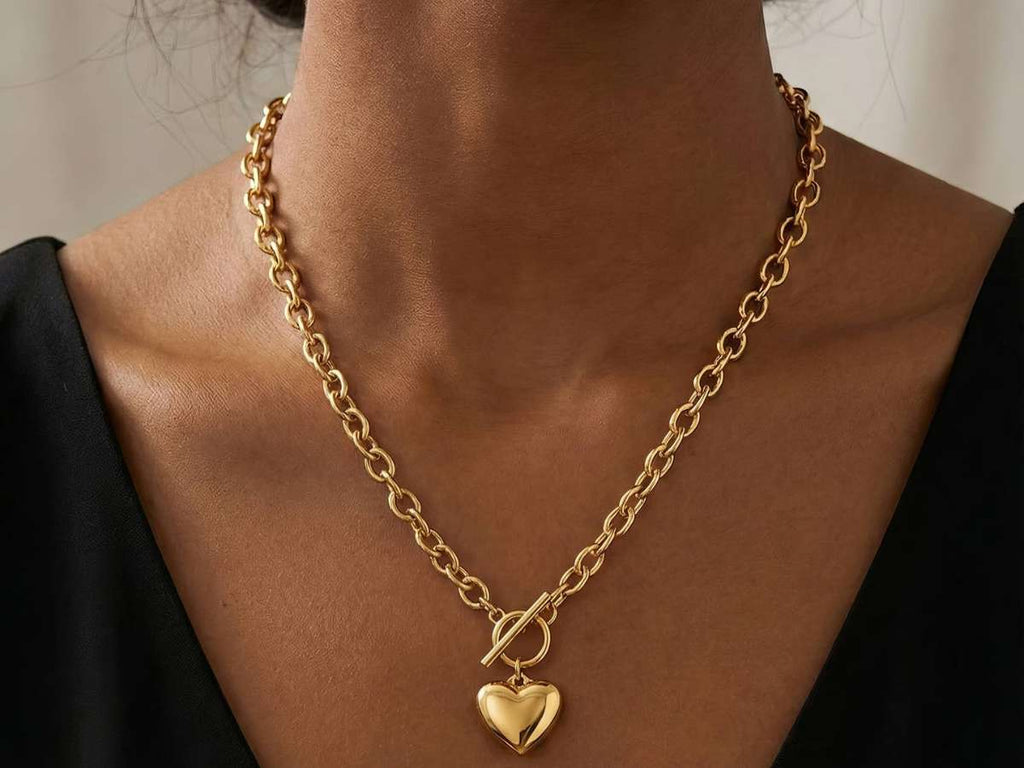 Gold chain necklace with a heart pendant on a person wearing a black top.