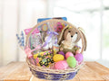 Easter gift basket with plush bunny, eggs, and candy on a wooden table.