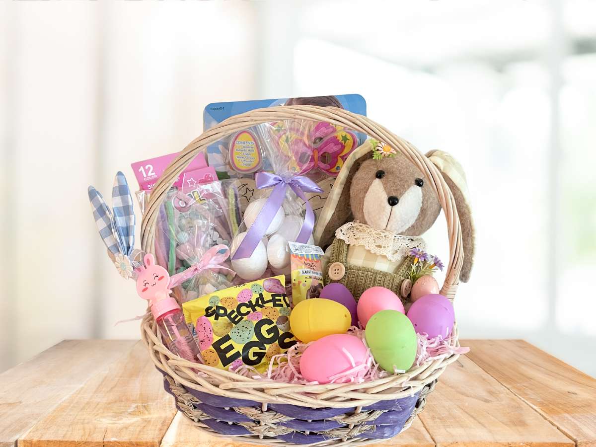 Easter gift basket with plush bunny, eggs, and candy on a wooden table.